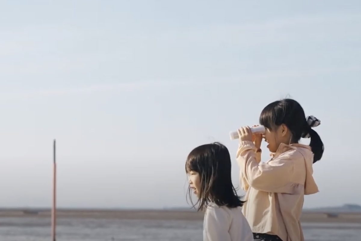 海辺で2人の女の子がREFの万華鏡を覗いているイメージ写真